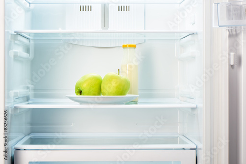 Apples on white plate with bottle of yoghurt in refrigerator