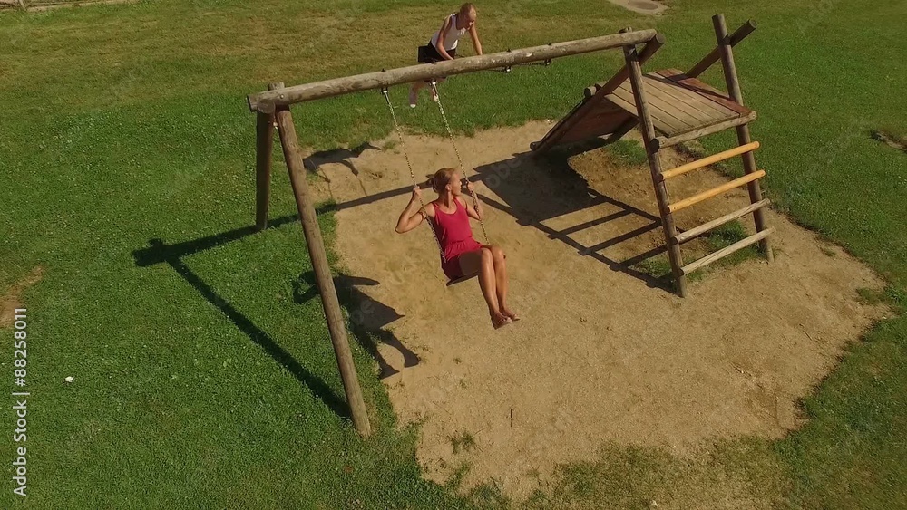 Two adorable girls having fun on a swings on summer day (aerial view) Two adorable girls having fun on a swings on summer day (aerial view)