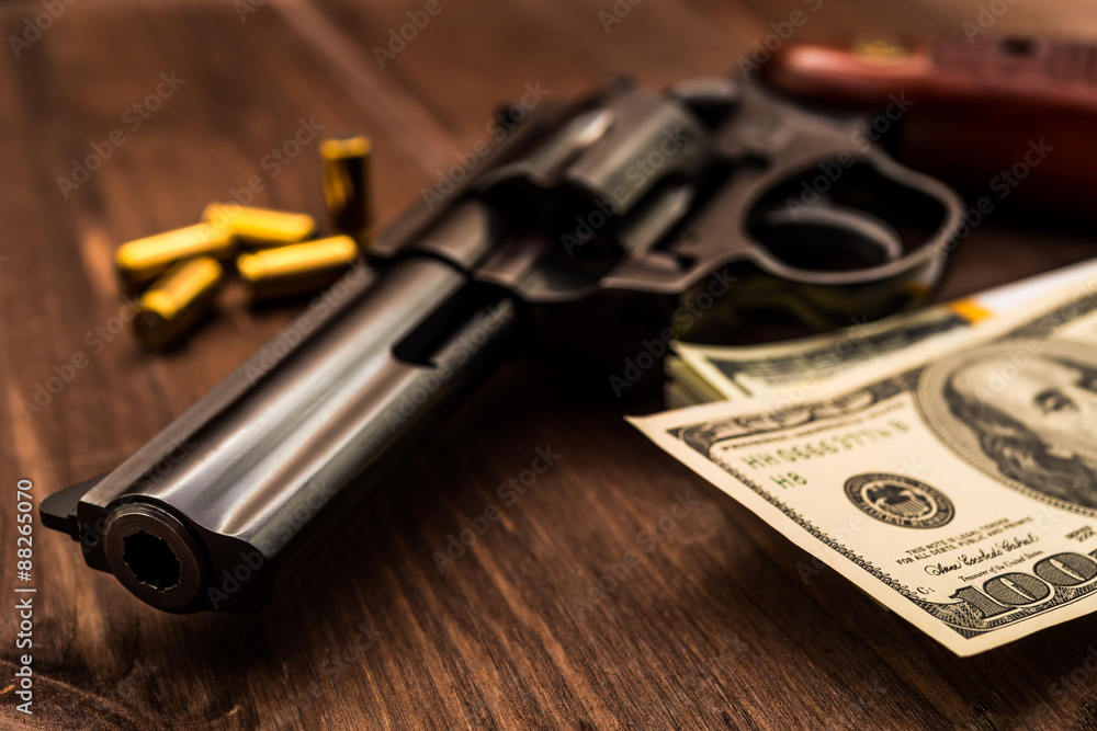 Revolver and pack of dollars with cartridges on the wooden table Revolver and pack of dollars with cartridges on the wooden table