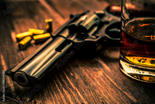 Glass of whiskey with revolver on the wooden table photo