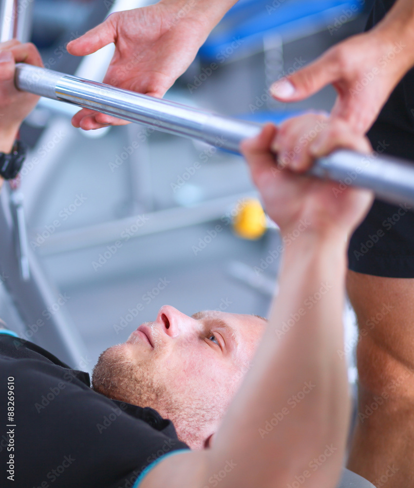 Fototapeta premium Young man lifting the barbell in gym with instructor