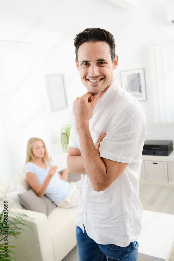 portrait of handsome young man at home with his girlfriend in background portrait of handsome young man at home with his girlfriend in background