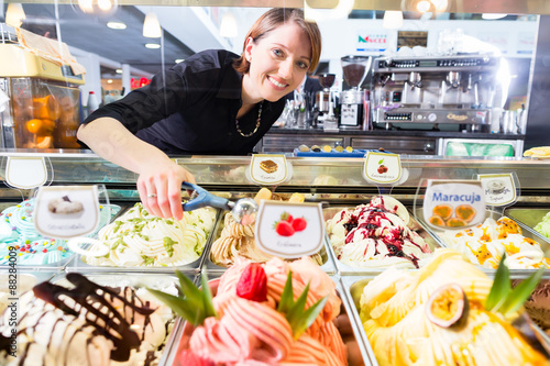 Verkäuferin in Eisdiele zeigt Eissorten in Vitrine photo