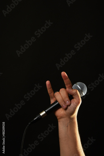 Hand with microphone and devil horns isolated on black