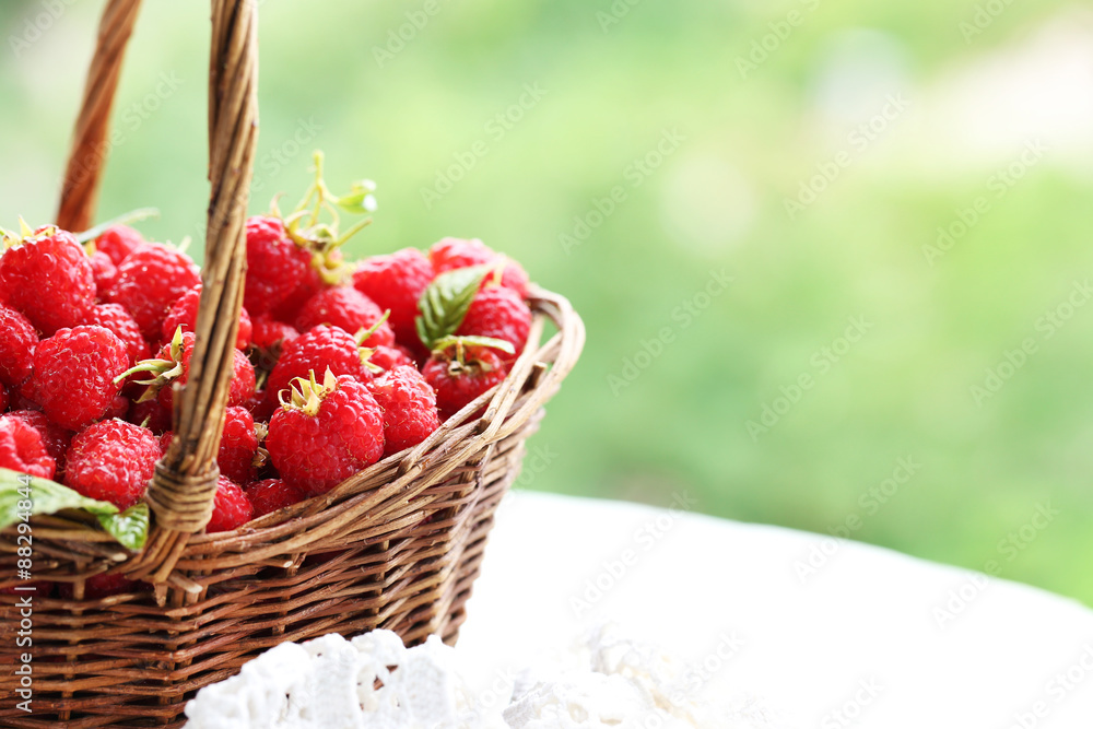 Fresh raspberries in wicker basket on wooden table on blurred nature background Fresh raspberries in wicker basket on wooden table on blurred nature background