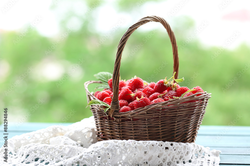 Fresh raspberries in wicker basket on wooden table on blurred nature background Fresh raspberries in wicker basket on wooden table on blurred nature background