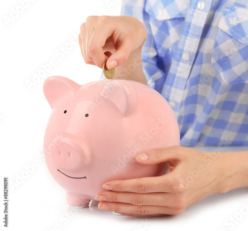 Female hands putting coin into pink piggy bank isolated on white