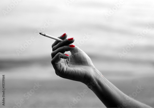 Женская рука с красным маникюром держит тоненькую сигарету (черно-белое фото)