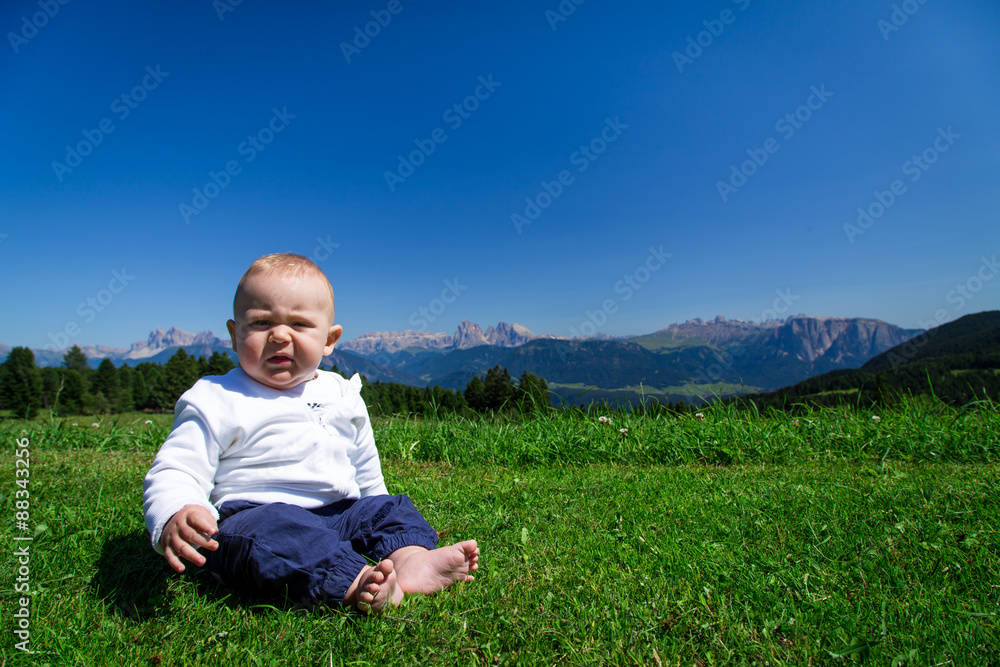 Cute baby sitting on green grass with Dolomiti panorama on background Cute baby sitting on green grass with Dolomiti panorama on background