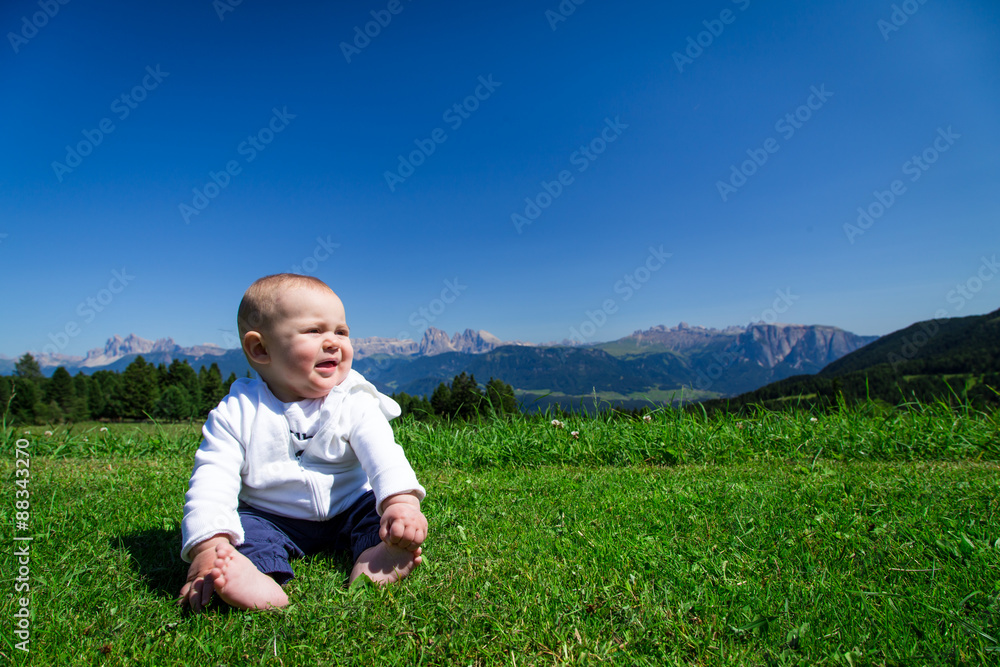 Cute baby sitting on green grass with Dolomiti panorama on background Cute baby sitting on green grass with Dolomiti panorama on background