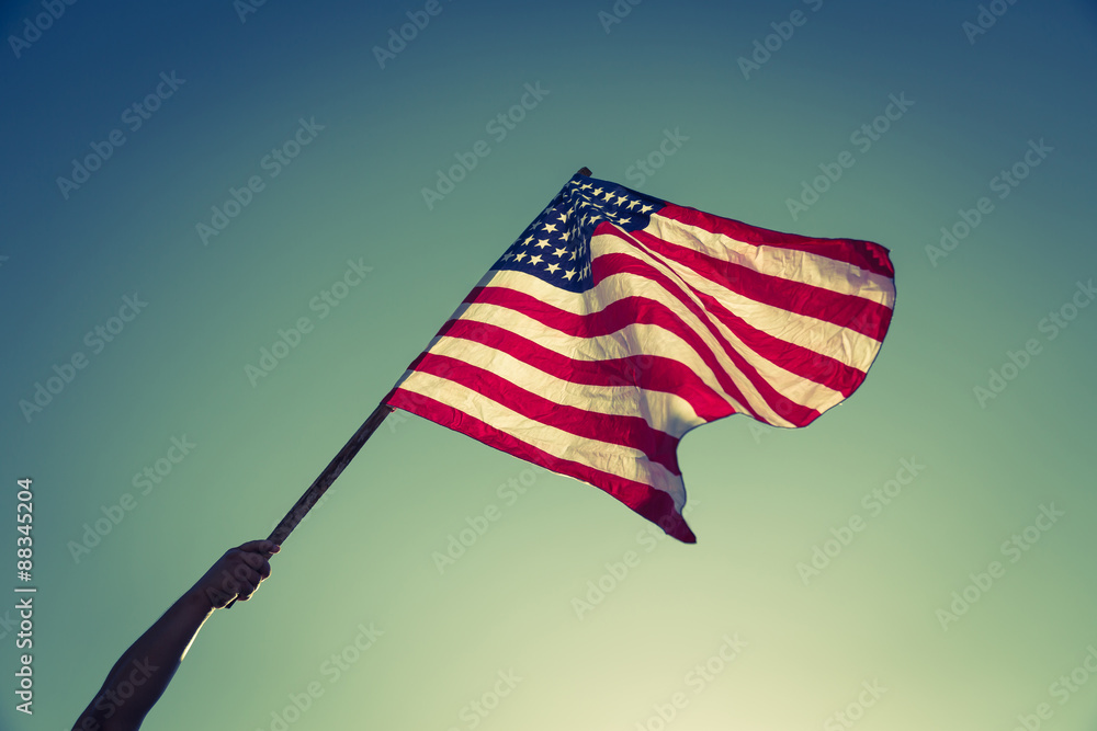 American flag with stars and stripes hold with hands against blu