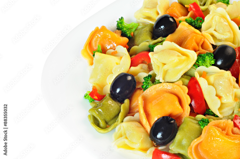 Salad made with tortellini, olives, broccoli, red pepper, on a plate, white background