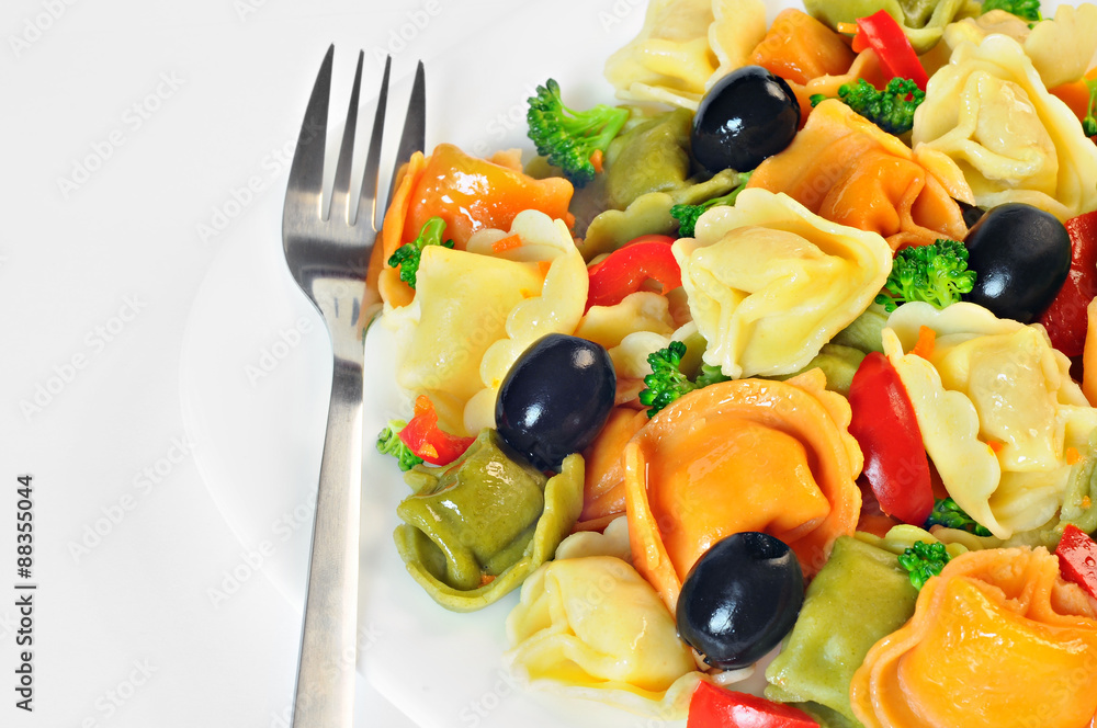 Salad made with tortellini, olives, broccoli, red pepper, on a plate with a fork, white background Salad made with tortellini, olives, broccoli, red pepper, on a plate with a fork, white background