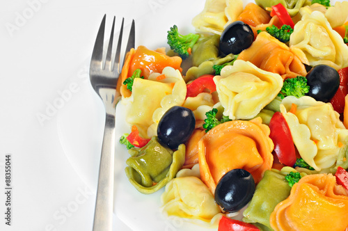 Salad made with tortellini, olives, broccoli, red pepper, on a plate with a fork, white background