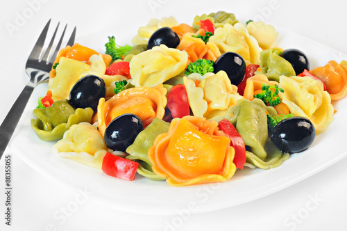 Salad made with tortellini, olives, broccoli, red pepper, on a plate with a fork, white background