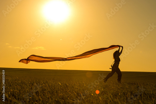 Young woman running on a rural road at sunset in summer field