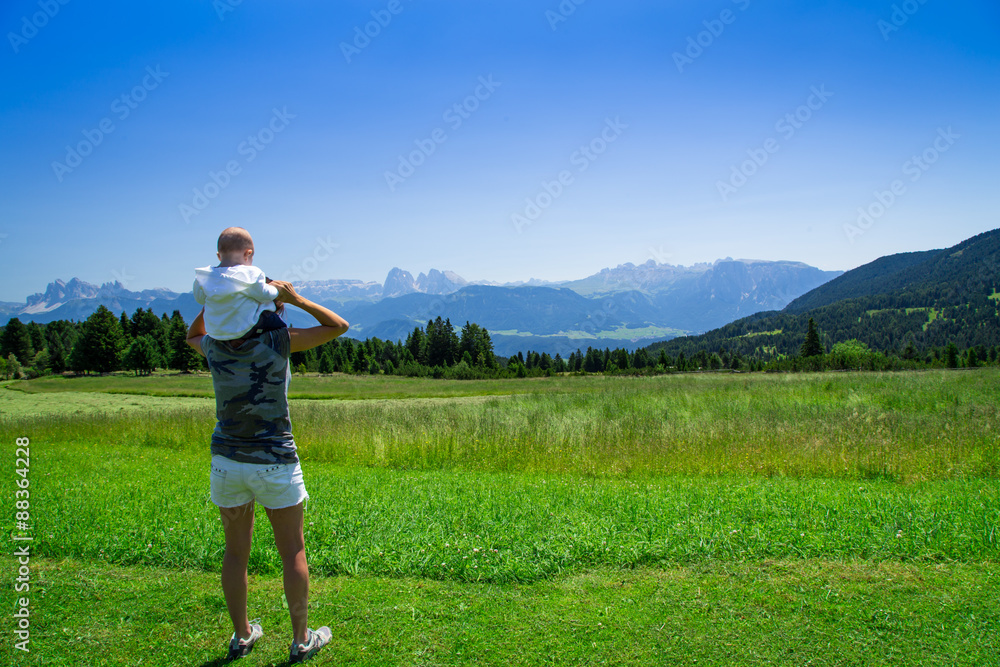 Cute baby sitting on mother shoulders looking the Dolomiti mountain