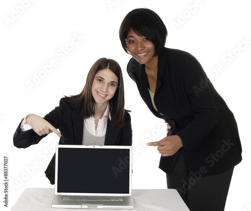 Two business women point to a blank laptop screen.