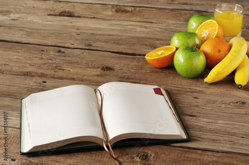 Fototapeta Naklejka Na Ścianę i Meble -  open notebook on wooden table with fruits and orange juice