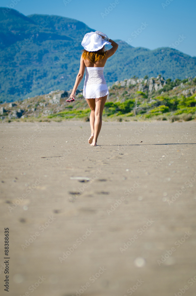beautiful young woman takes a relaxing walk along a sandy beach 
