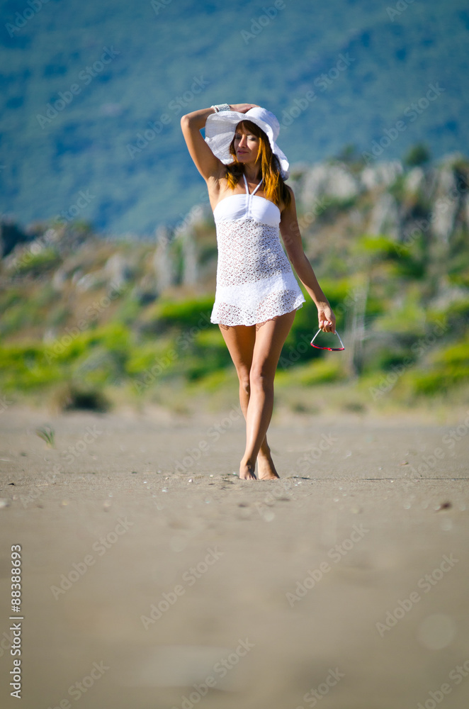 beautiful young woman takes a relaxing walk along a sandy beach 
