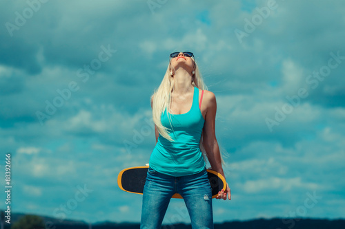 Young trendy girl in jacket sitting on a skateboard on the background of wall. Outdoor lifestyle portrait