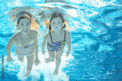 Children swim in pool underwater, happy active girls have fun in water