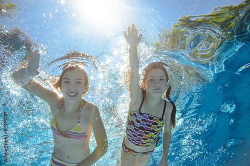 Children swim in pool underwater, happy active girls have fun in water 