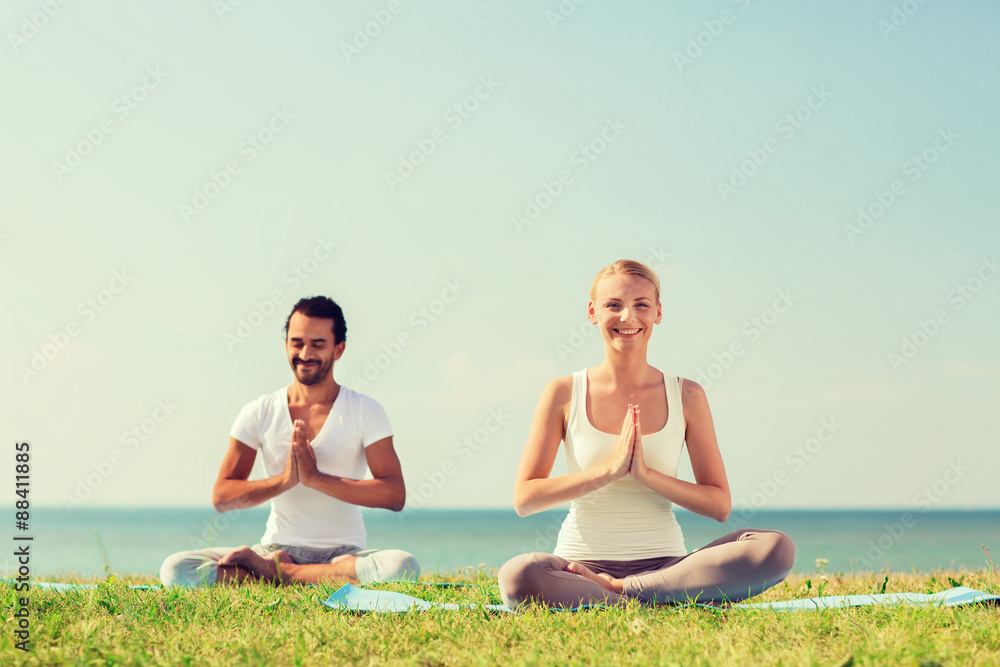 smiling couple making yoga exercises outdoors