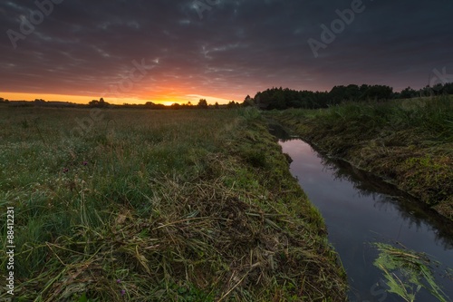 Beautiful sunrise over misty meadow and stream