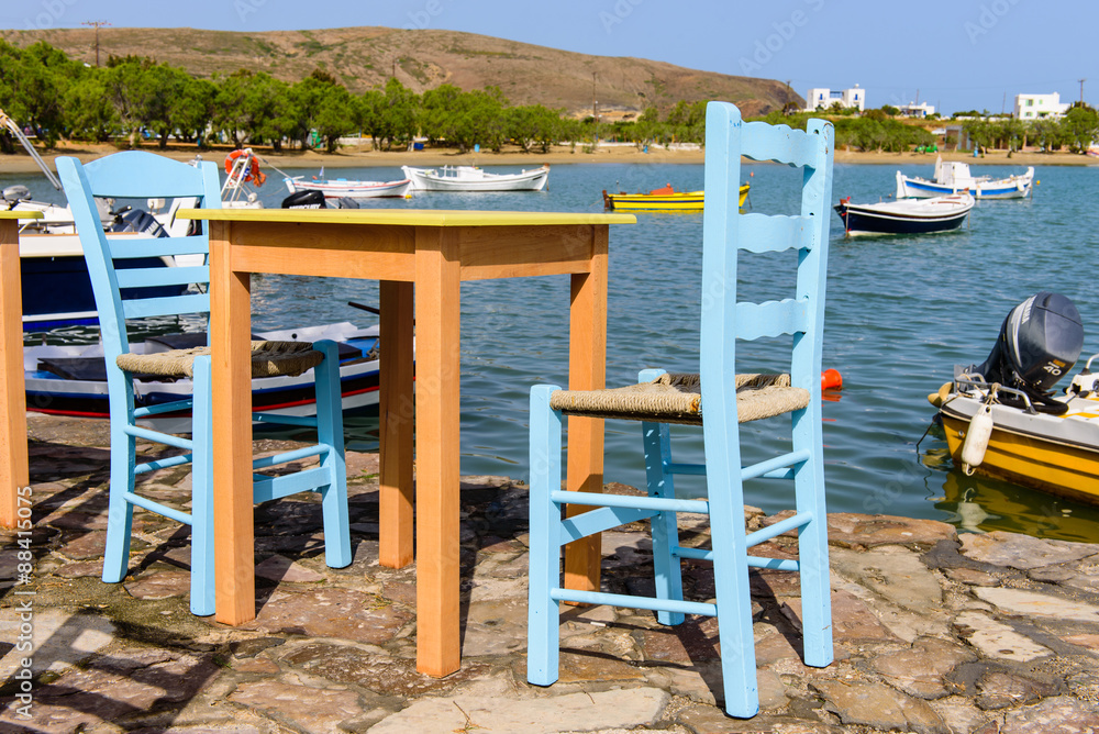 Traditional Greek taverna on the seafront on the beach - bright chairs and table, Pollonia village, Milos island, Cyclades, Greece. Traditional Greek taverna on the seafront on the beach - bright chairs and table, Pollonia village, Milos island, Cyclades, Greece.