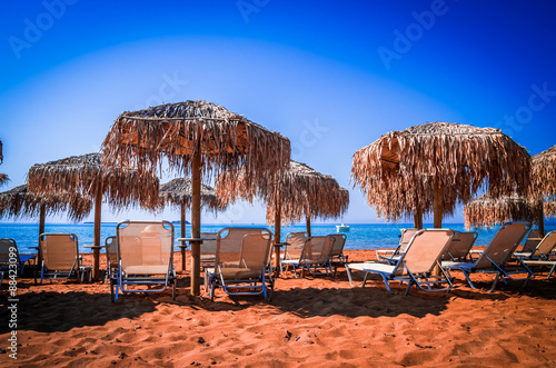 Straw umbrellas and sunbeds on a sandy beach in Greece. Parasols and tanning beds on the beach. 