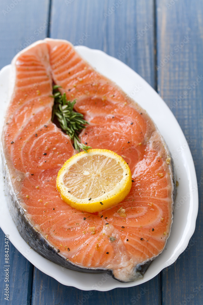 fresh salmon with lemon on white dish on blue wooden background