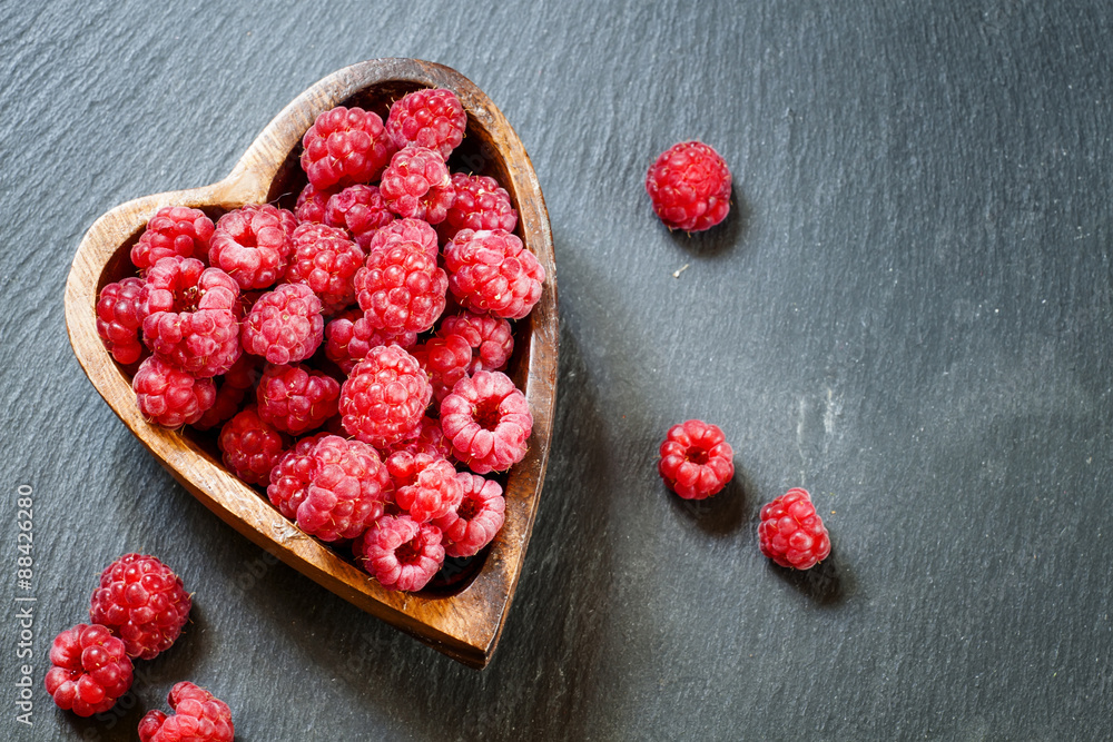Fresh raspberries in a bowl in the shape of a heart on a dark ba Fresh raspberries in a bowl in the shape of a heart on a dark ba