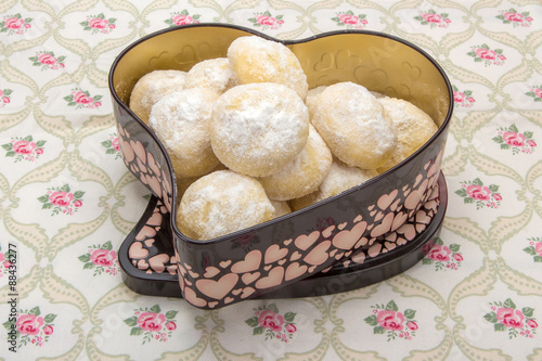 Small cookies in powdered sugar in a tin box on cotton napkin with floral pattern