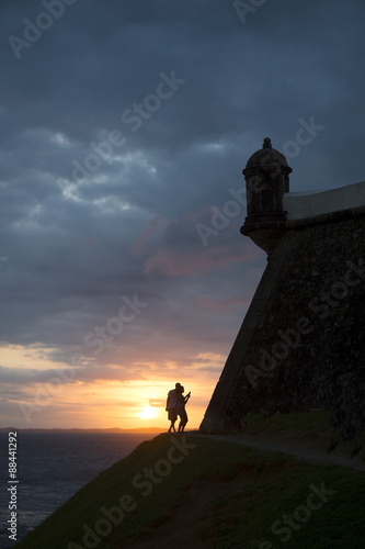 Silhouette of couple taking a sunset selfie in front of the view of the Bay of All Saints from the Farol da Barra lighthouse in Salvador, Bahia, Brazil