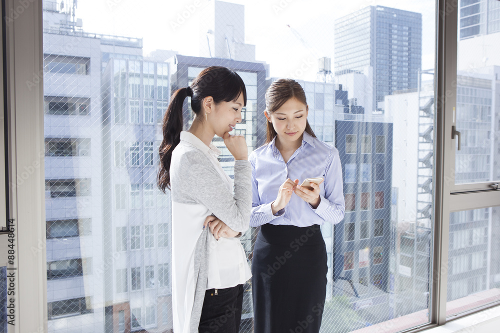 Obraz premium Two women looking at a mobile phone at the window