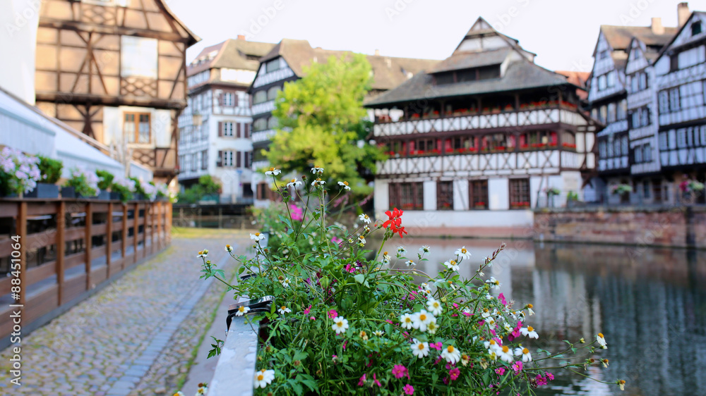 Medieval cityscape of timber-framed buildings in the Petite-France district alongside the river Ill on sunny summer day. Focus on flowers on the bridge. France, Alsace region, Strasbourg