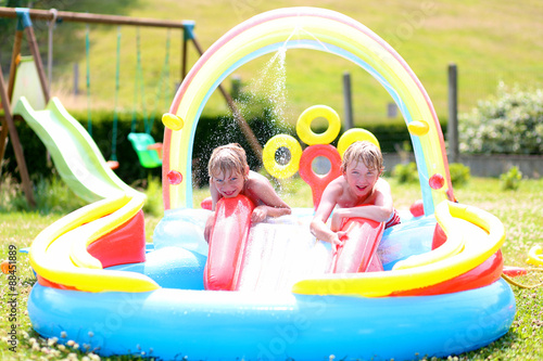 Group of happy healthy kids having fun in inflatable play centre. Children enjoying summer holidays playing in the pool at the backyard in the garden. © cromary