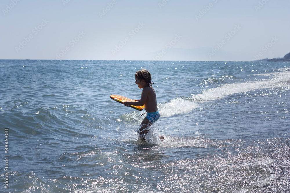 Niño con tabla de surf en la orilla del mar Stock Photo | Adobe Stock
