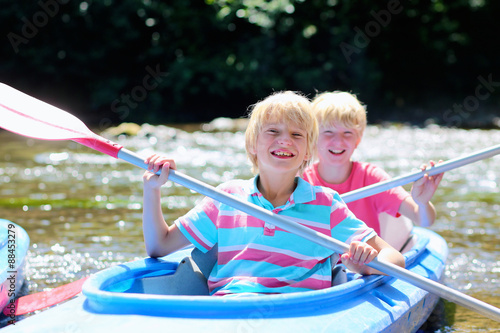 Two happy kids kayaking on the river. Active happy twin brothers, teenage school boys, having fun together enjoying adventurous experience on a sunny day during summer vacation.