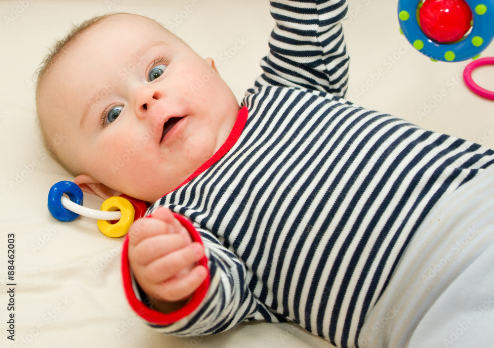Infant boy with wide opened blue eyes laying on a blanket with plastic bright rattles Infant boy with wide opened blue eyes laying on a blanket with plastic bright rattles