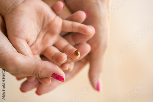 Mothers hand cupping her childs hand on which ladybug is sitting