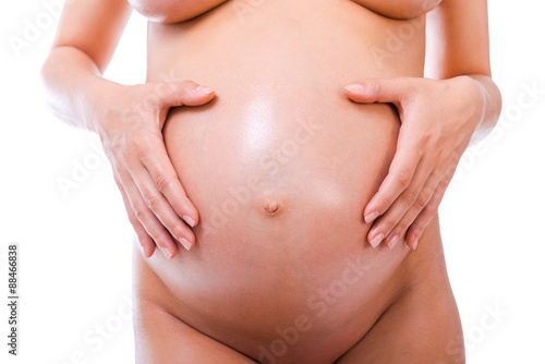 Pregnant belly. Close-up of pregnant woman holding hands on her abdomen while standing against white background