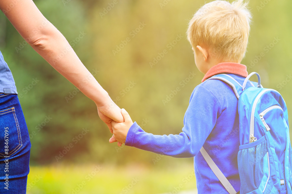 Naklejka premium Mother holding hand of little son with backpack outdoors