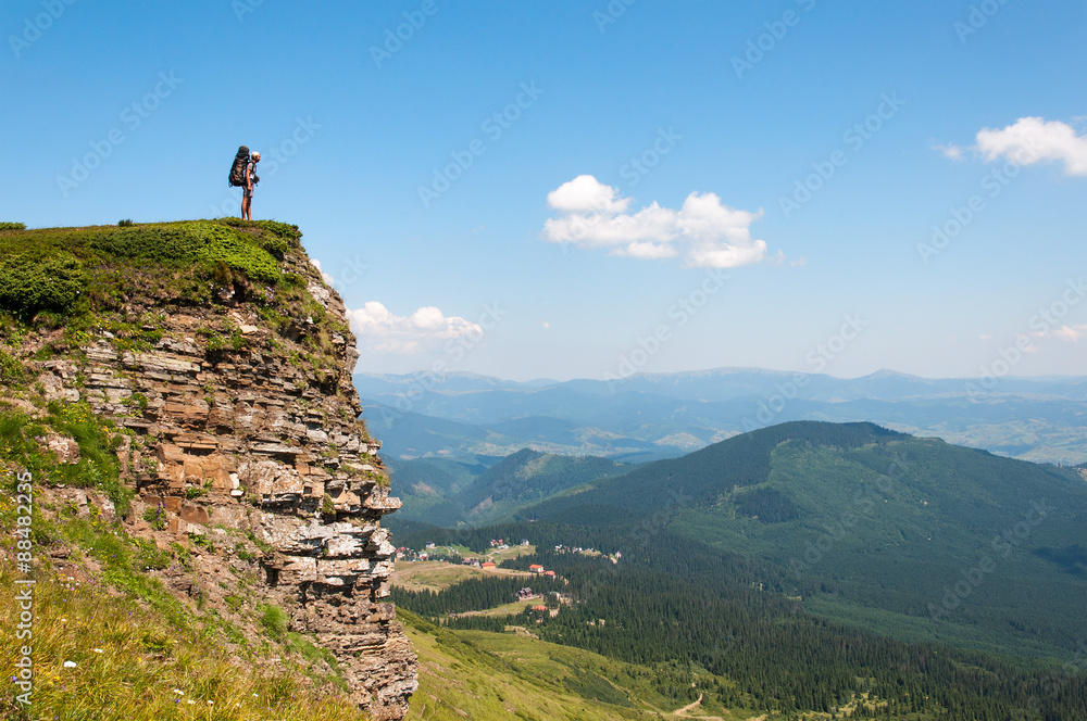 Backpacker man standing on a high rock 