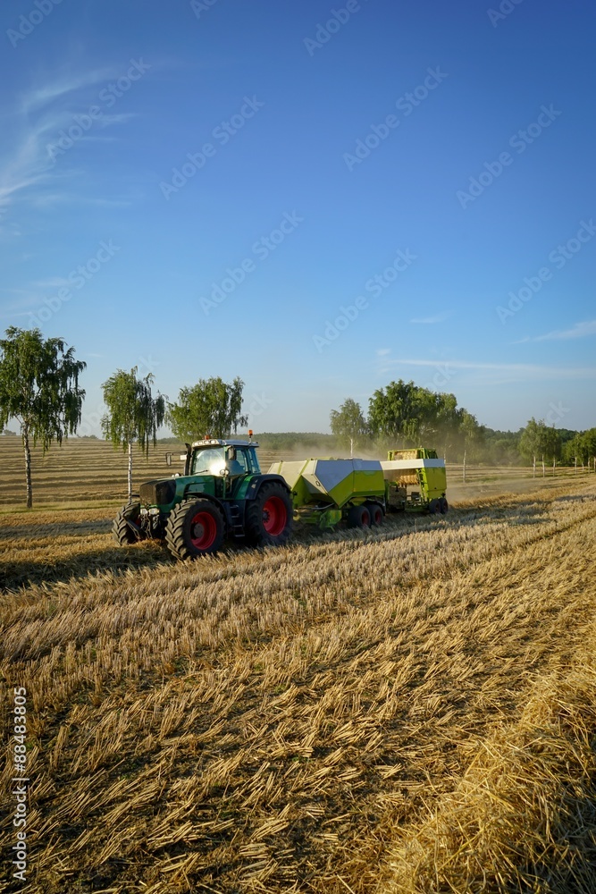 Obraz premium Strohernte, Traktor mit Ballenpresse und Ballenstapler