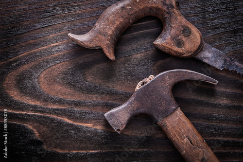 Rusty metal handsaw with claw hammer on vintage dark wooden boar