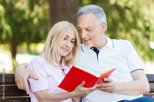 senior couple reading a book while sitting on the park bench