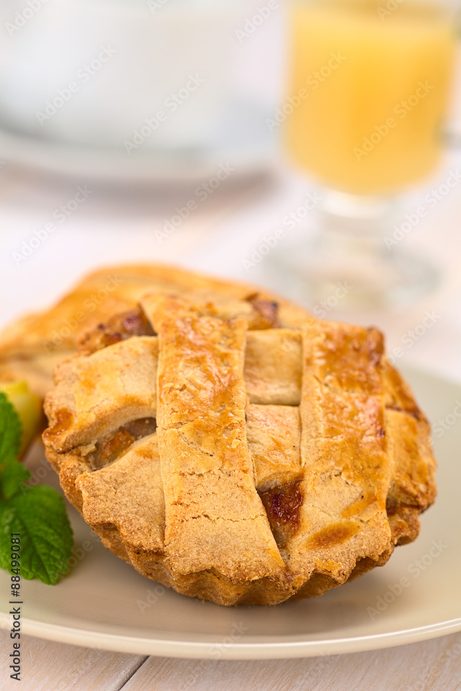Small round apple pie with lattice crust with mint leaf on a plate, hot apple punch in the back (Selective Focus, Focus one third into the pie) Small round apple pie with lattice crust with mint leaf on a plate, hot apple punch in the back (Selective Focus, Focus one third into the pie)